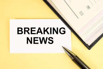 breaking news. the text WRITTEN on a white sheet of paper on a yellow background near a notebook and a pen