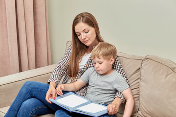 Young brunette mom teaches her preschool son while sitting at home on the couch.