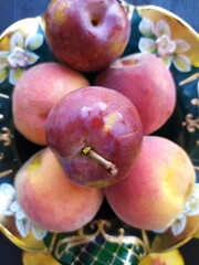 Food still life with fruits ripe peach red plums on a green bowl on the black wooden table