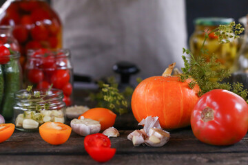 Metal jar sealer tool closeup. Lid closer for glass preserves and homemade vegetables - tomatoes, pumpkin, zucchini, greens and olive oil bottle on wooden table. Food preservation during crisis