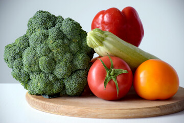 Assortment of healthy food ingredients for cooking on a wooden cutting board. Organic vegetables: broccoli, tomato, zucchini and pepper. Balanced nutrition or dieting concept.