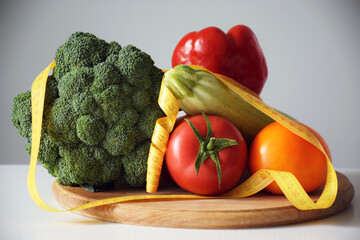 Assortment of fresh vegetables and measuring tape on wooden cutting board. Balanced nutrition, healthy eating, weight loss, detox or dieting concept.