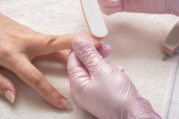 Manicurist filing client's nails at table, closeup. Manicure process in beauty salon, close up. Woman in nail salon receiving manicure by beautician.