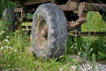 Fototapeta na wymiar An abandoned old cargo trailer stands in a field on green grass. Trailer wheel and chassis close up