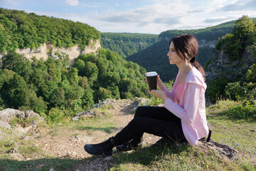 Naklejka na ściany i meble Young woman sitting and drink coffee on the mountains