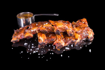Delicious marinated pork ribs and sauce vide,  with reflection, isolated on black background