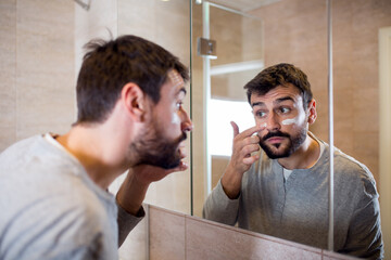 Beard man applying hydrating cream on face in bathroom