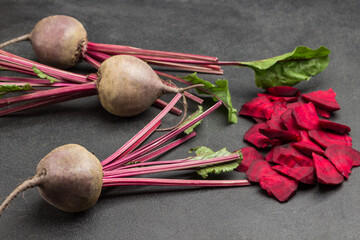 Beets with tops, sliced beets on black background.