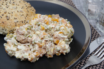Tuna salad in black plate. Ingredients: tuna, carrots, eggs, onion, canned peas, croutons, mayonnaise