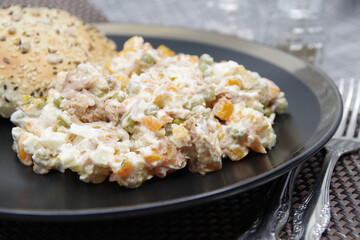 Tuna salad in black plate. Ingredients: tuna, carrots, eggs, onion, canned peas, croutons, mayonnaise