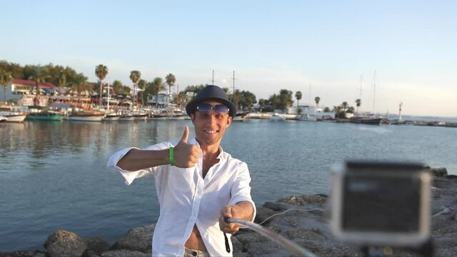 Young man taking selfie picture posing with thumbs up sign and smiling. Holidays, beach resort, taking vacation pictures concept.