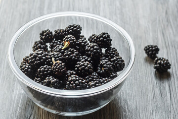 Fototapeta na wymiar Berries of fresh ripe blackberries in a glass bowl on a gray wooden background. Healthy summer berries. Healthy vegetarian food. Background with blackberries and free space.