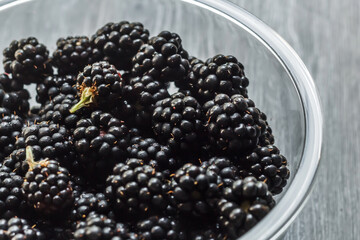 Fresh ripe blackberries in a glass bowl on a gray wooden background close up. Healthy summer berries. Healthy vegetarian food. Background with blackberries and free space.