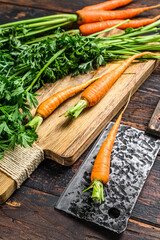 Fresh carrots with green leaves on a cutting board. Wooden background. Top view