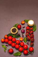 Ripe cherry tomatoes, garlic, basil, salt and black peppercorns on a black stone culinary background