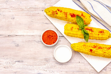 Boiled corn cobs on ceramic plate. Sea salt, fragrance paprika, fresh basil leaf