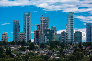 Fototapeta na wymiar Construction of New Residential District in the city of Burnaby, high-rise buildings under construction and construction cranes against the backdrop of blue cloudy sky and village in the foreground