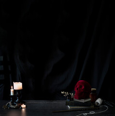 witch or wizards desk, smoking candles on library table with vintage books, magic wand and other halloween decor, and a dark background with copyspace