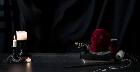 witch or wizards desk, smoking candles on library table with vintage books, magic wand and other halloween decor, and a dark background with copyspace