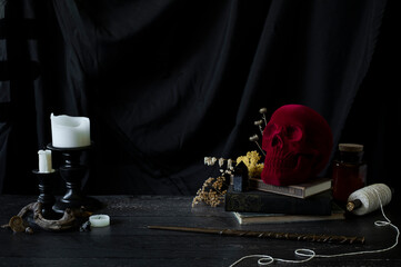 witch or wizards desk, smoking candles on library table with vintage books, magic wand and other halloween decor, and a dark background with copyspace