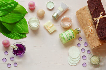 Obraz na płótnie Canvas Green fresh leaves on the background of organic cosmetics. Towels, cotton pads, pink cream, green gel, handcrafted soap, natural, foot care, pedicure, healthy feet