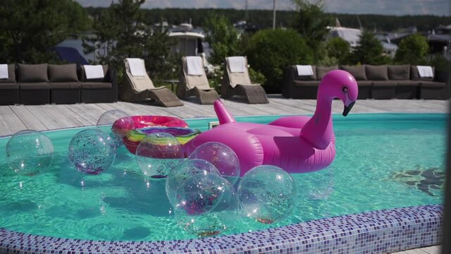 Inflatable pink flamingo, balls with sparkles and a circle floats in the pool with blue water. Summer vacation and fun time in the swimming pool
