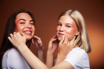 two pretty diverse girls happy posing together: blond and brunette on brown background, lifestyle people concept