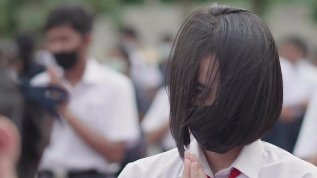 Slow motion female Asian high school student in white uniform on the semester start wearing masks and stand in line to pray in the morning during the Coronavirus 2019 (Covid-19) epidemic.