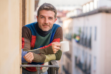 30s or 40s attractive and happy man at home balcony relaxed and cheerful enjoying cup of coffee looking to city street smiling and enjoying the urban view