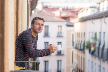 30s or 40s attractive and happy man at home balcony relaxed and cheerful enjoying cup of coffee smoking cigarette looking to city street smiling and enjoying the urban view