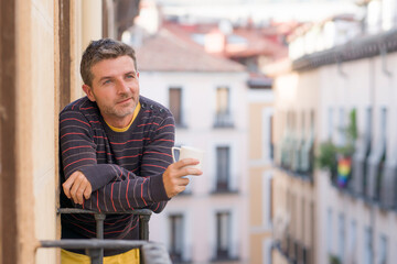 30s or 40s attractive and happy man at home balcony relaxed and cheerful enjoying cup of coffee looking to city street smiling and enjoying the urban view