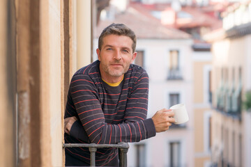 30s or 40s attractive and happy man at home balcony relaxed and cheerful enjoying cup of coffee looking to city street smiling and enjoying the urban view