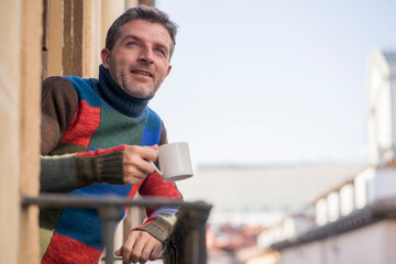 30s or 40s attractive and happy man at home balcony relaxed and cheerful enjoying cup of coffee looking to city street smiling and enjoying the urban view