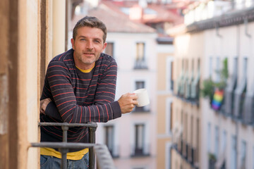 30s or 40s attractive and happy man at home balcony relaxed and cheerful enjoying cup of coffee looking to city street smiling and enjoying the urban view