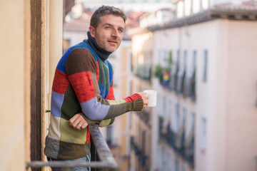 30s or 40s attractive and happy man at home balcony relaxed and cheerful enjoying cup of coffee looking to city street smiling and enjoying the urban view