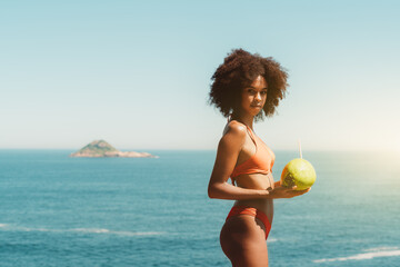 A hottie young African-American woman with curly afro hair is standing in front of a seascape and...