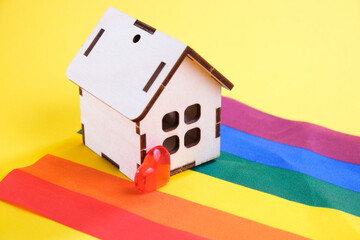 september and small wooden house on the lgbt flag, yellow background, copy space, same-sex love and life together same-sex families concept