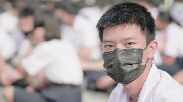 Slow motion of male Asian high school student in white uniform on the semester start wearing masks turn his face to look straight in the morning during the Coronavirus 2019 (Covid-19) epidemic.
