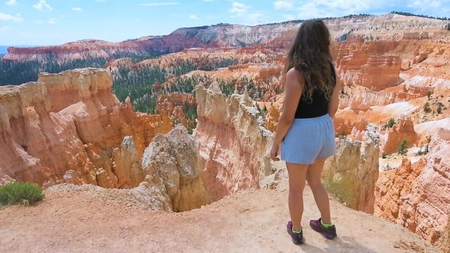 Woman person standing looking at view happy in slow motion from overlook cliff at Bryce Canyon National Park in Utah on Queens Garden Navajo Loop hiking trail