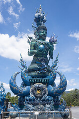 Chiangrai, Thailand - June 7, 2020: Blue God Statue Hold Lotus and Ball on Blue Sky Background with Natural Light in Wat Rong Suea Ten Temple at Side View