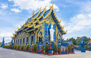 Chiangrai, Thailand - June 7, 2020: White Standing Buddha and Wat Rong Suea Ten Blue Yellow Church on Sky Background