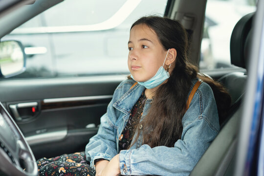 Teenager Girl Sitting In The Car With Medical Mask On Her Chin. Girl With Backpack On Her Back, Back To School Concept. Travel In The Car.