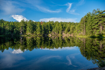 Obraz na płótnie Canvas Peaceful reflections - lake reflecting forest and clouds