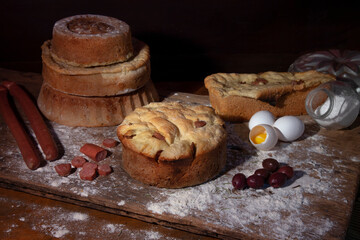 artisan breads on a wooden table dirty with flour and with ingredients olives, eggs and sausage and rosemary.