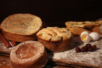 artisan breads on a wooden table dirty with flour and with ingredients olives, eggs and sausage and rosemary.