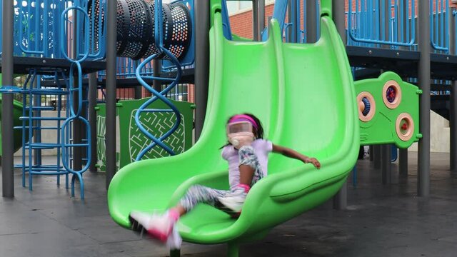 Little Black Girl playing on Playground  slide in park on summer day