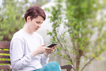 A girl in home clothes sitting on a bench with a smartphone in her hand