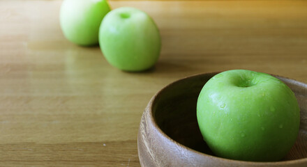 Green apple in wooden bowl on oak wood table
