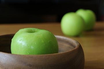 Green apple in wooden bowl on oak wood table