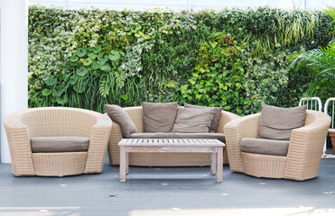 Luxury brown rattan patio garden and hotel furniture chairs and table with the earth-tone pillow set on it and green bush background for recreational, relaxation and resting. 